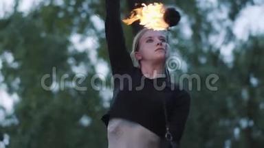 金发自信的女人在森林或公园里用火焰表演节目的肖像。 有技巧的消防艺术家
